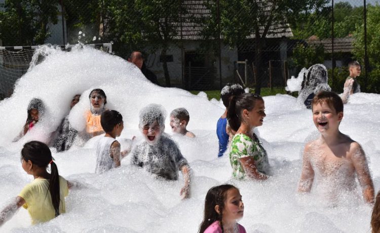 Children having fun in a foam party outdoors during summer.